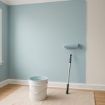 Interior of a room with blue and beige walls, a paint roller, and a bucket of paint